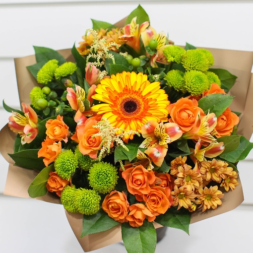 Оранжево-зеленый букет из кустовых роз, хризантемы сантини, альстромерий и астильбы в матовой бумаге цвета темного золота