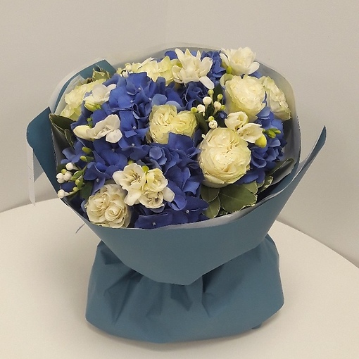 Букет-пирожное из голубой гортензии, ароматной фрезии, белых роз и декоративной зелени-бовардии.